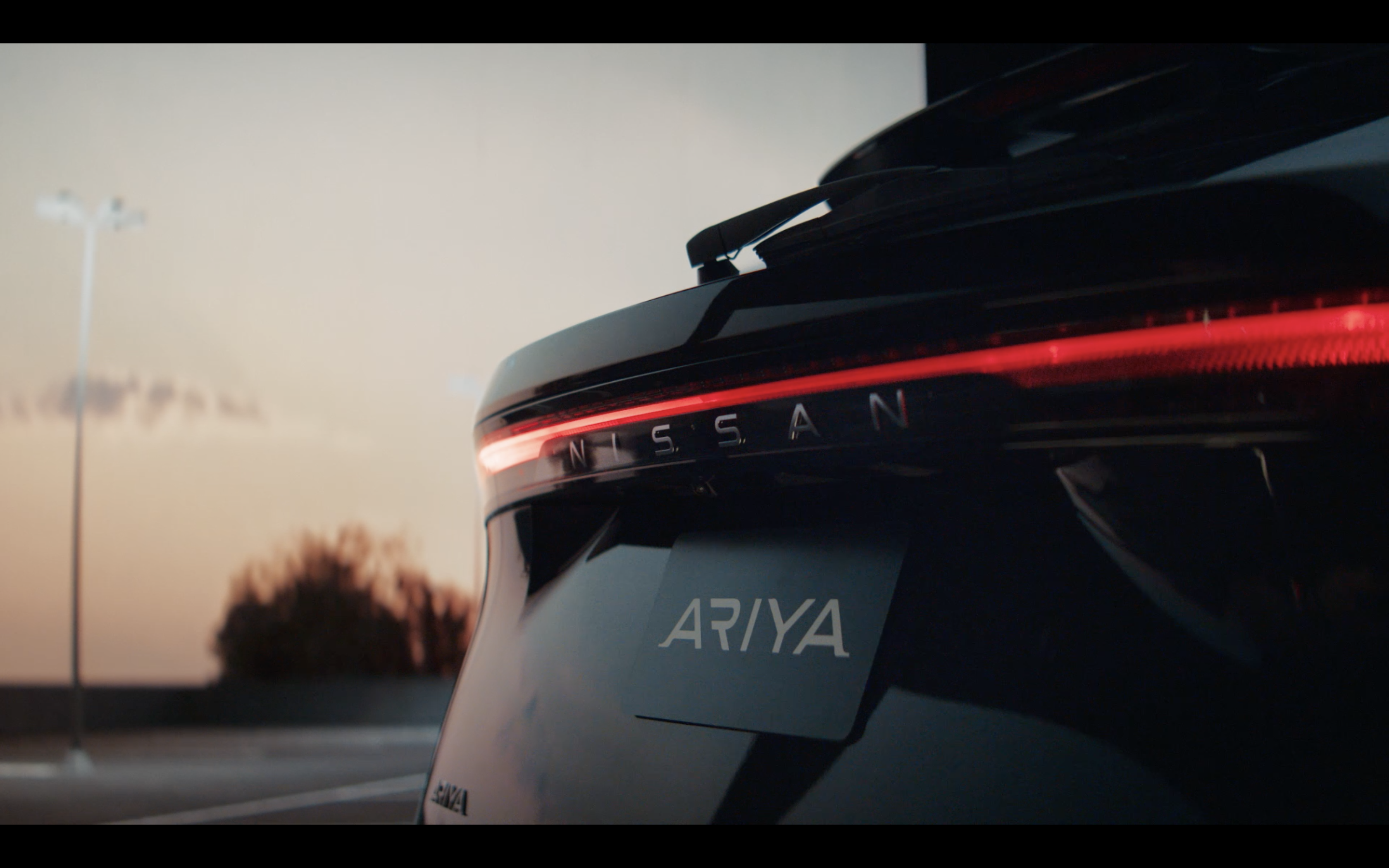 Rear view of a Nissan ARIYA at dusk, showcasing the car's sleek taillight design